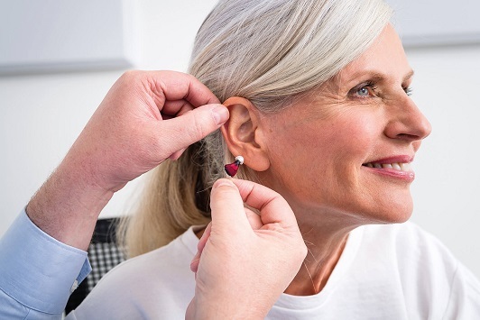 Ältere Frau bekommt ein modernes Hörgerät eingesetzt, Hörakustik und Hörhilfe-Beratung.